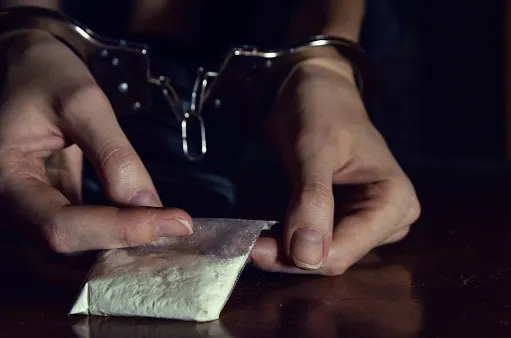 A juvenile handcuffed and holding a small bag with white powder.