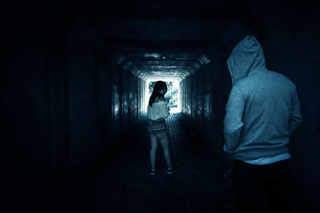 A person wearing a grey hoodie sweatshirt following a young women through a tunnel.