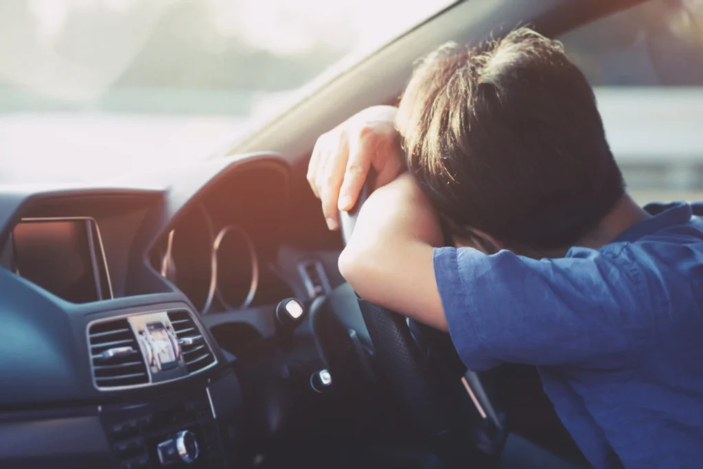 A drunk driver asleep on the steering wheel of a car.