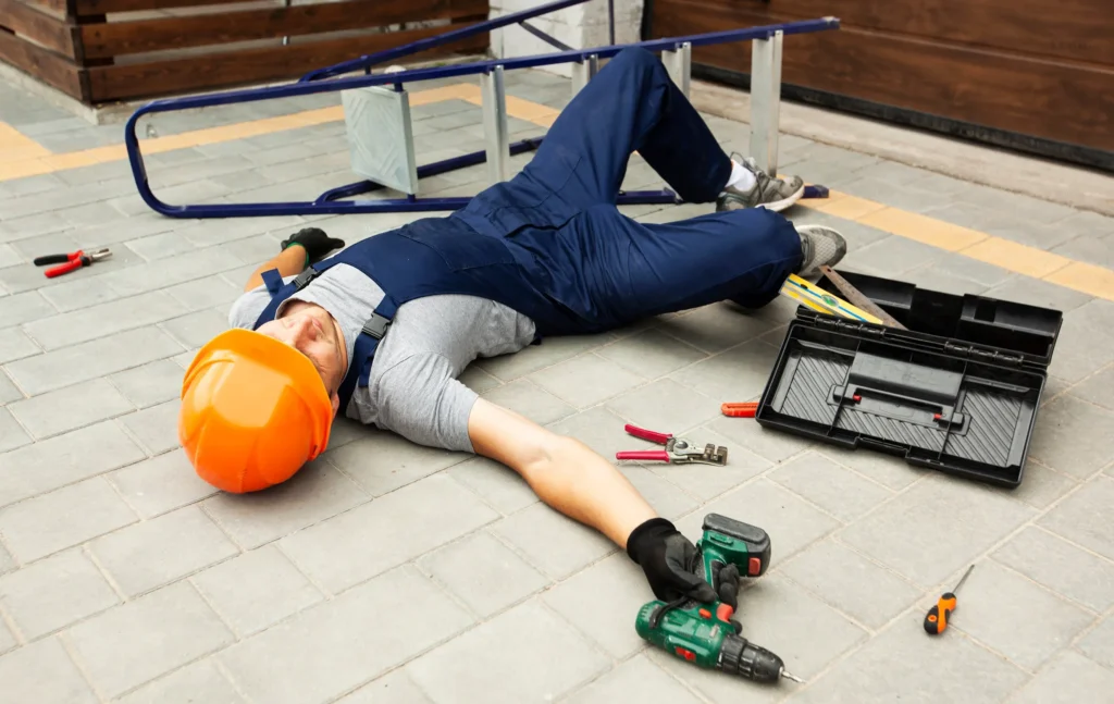 Worker wearing an orange construction hat, laying on the floor after falling.