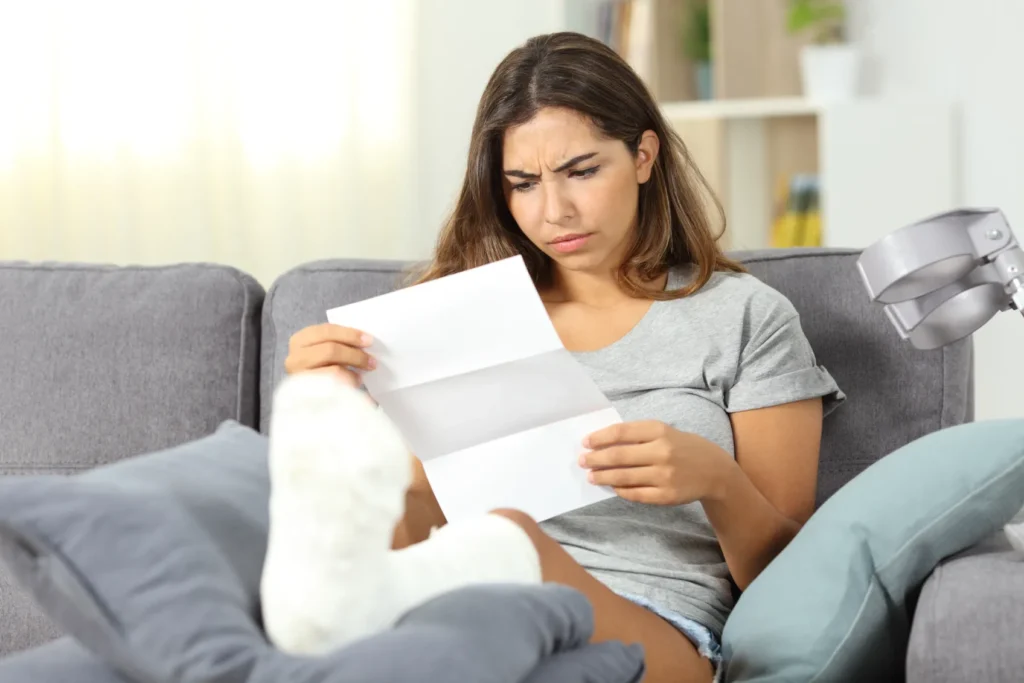 Women with leg in cast, sitting on a couch, looking at a document.